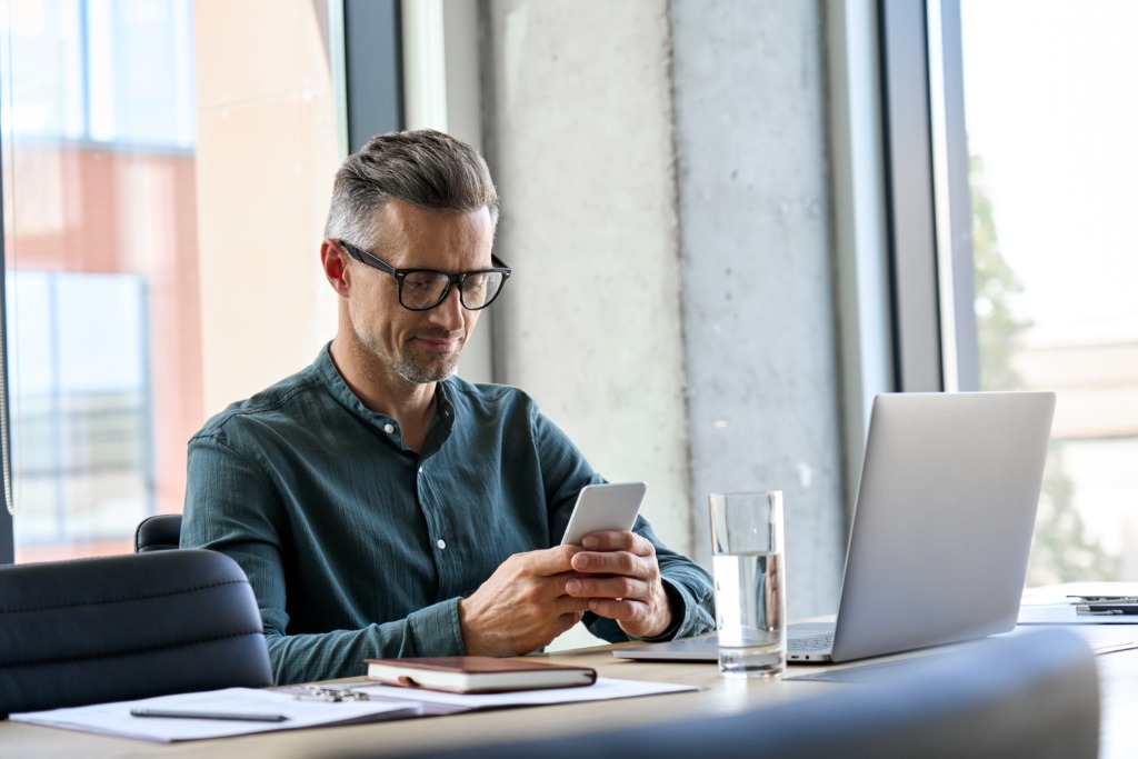 Business man, sat at desk, dialling phone number into mobile phone