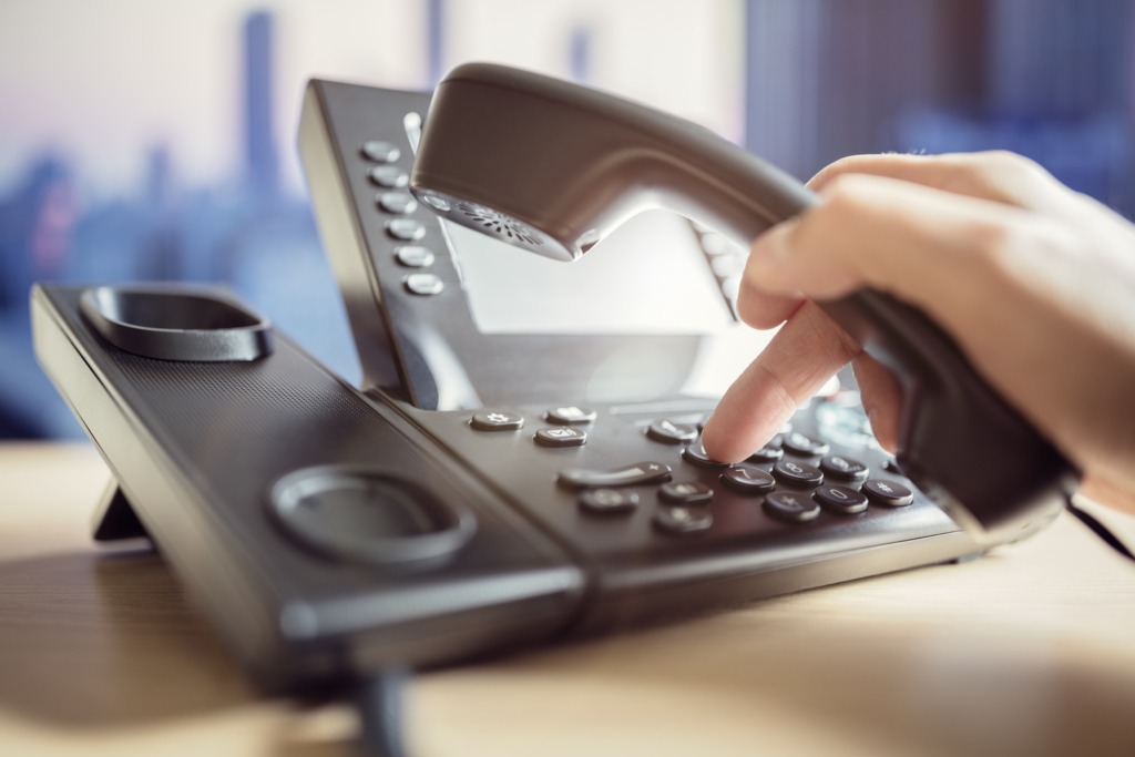 Hand holding receiver of a landline phone handset, dialling phone number into keypad