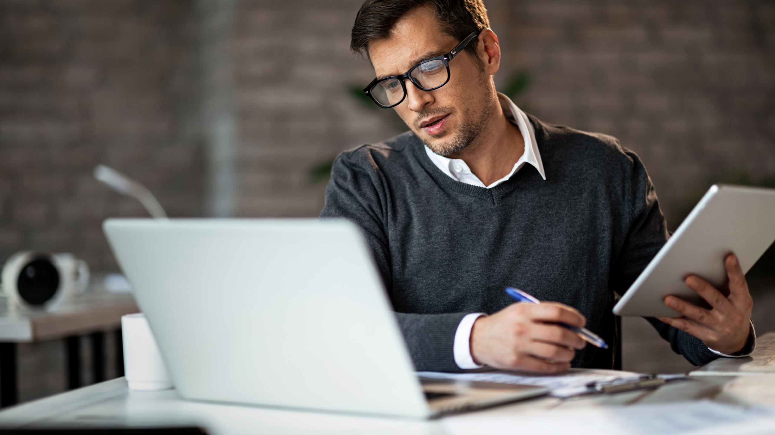 Male business owner working from ipad and laptop and making notes. 