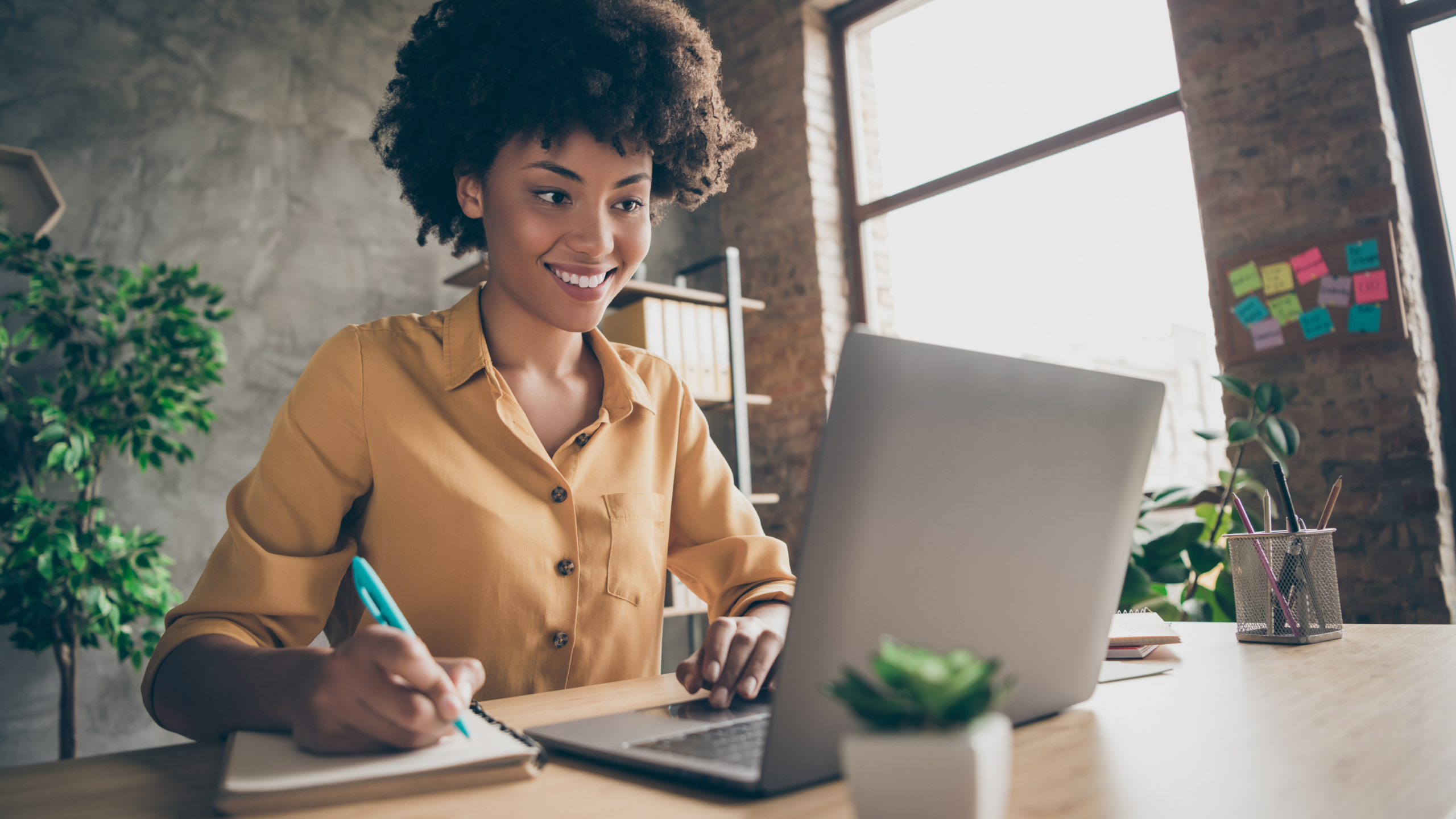 Professional woman writing notes on cyber security training while working on a laptop