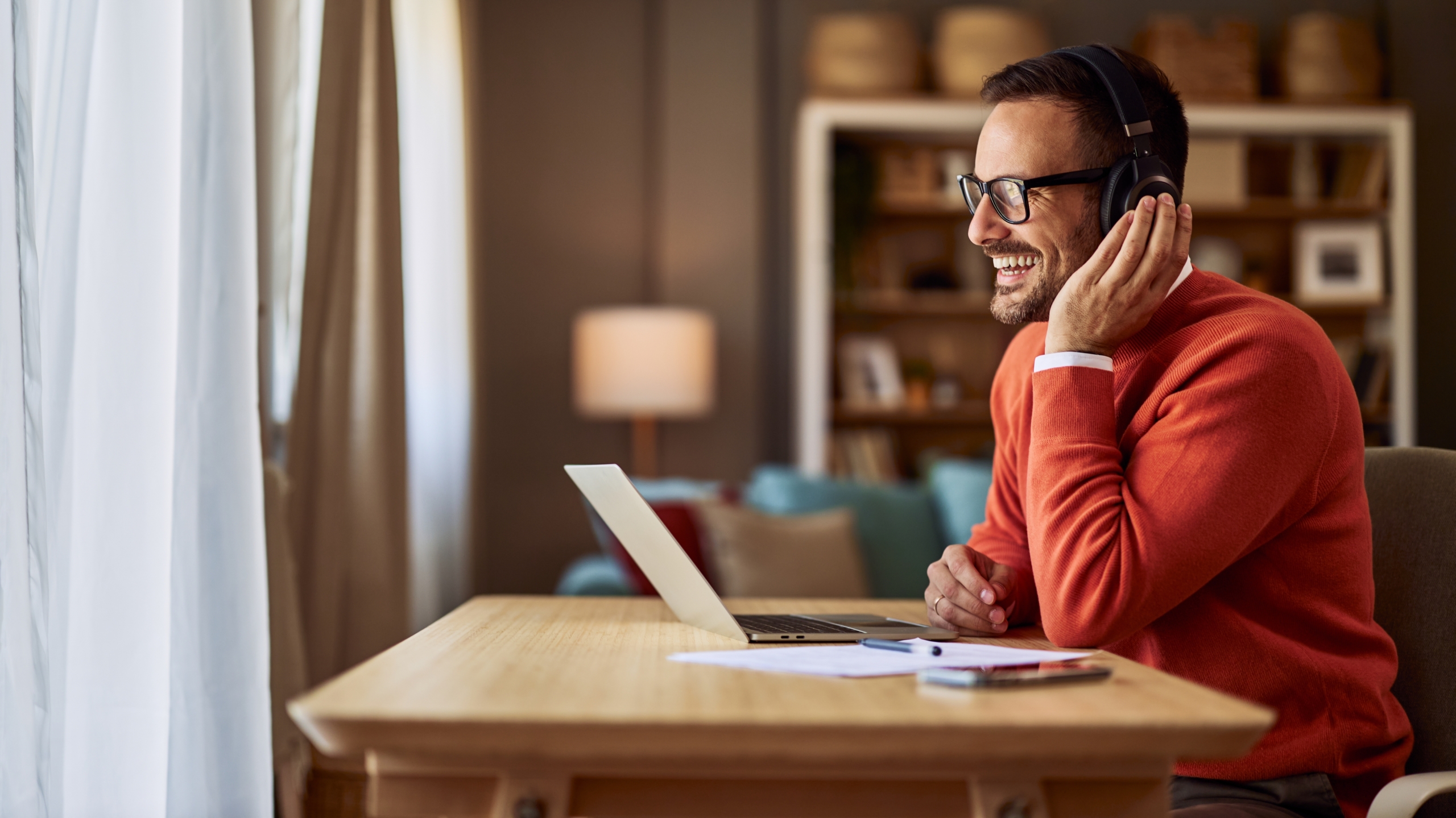 Home worker wearing headphones smiling during a call using a unified communications solution on a laptop. 