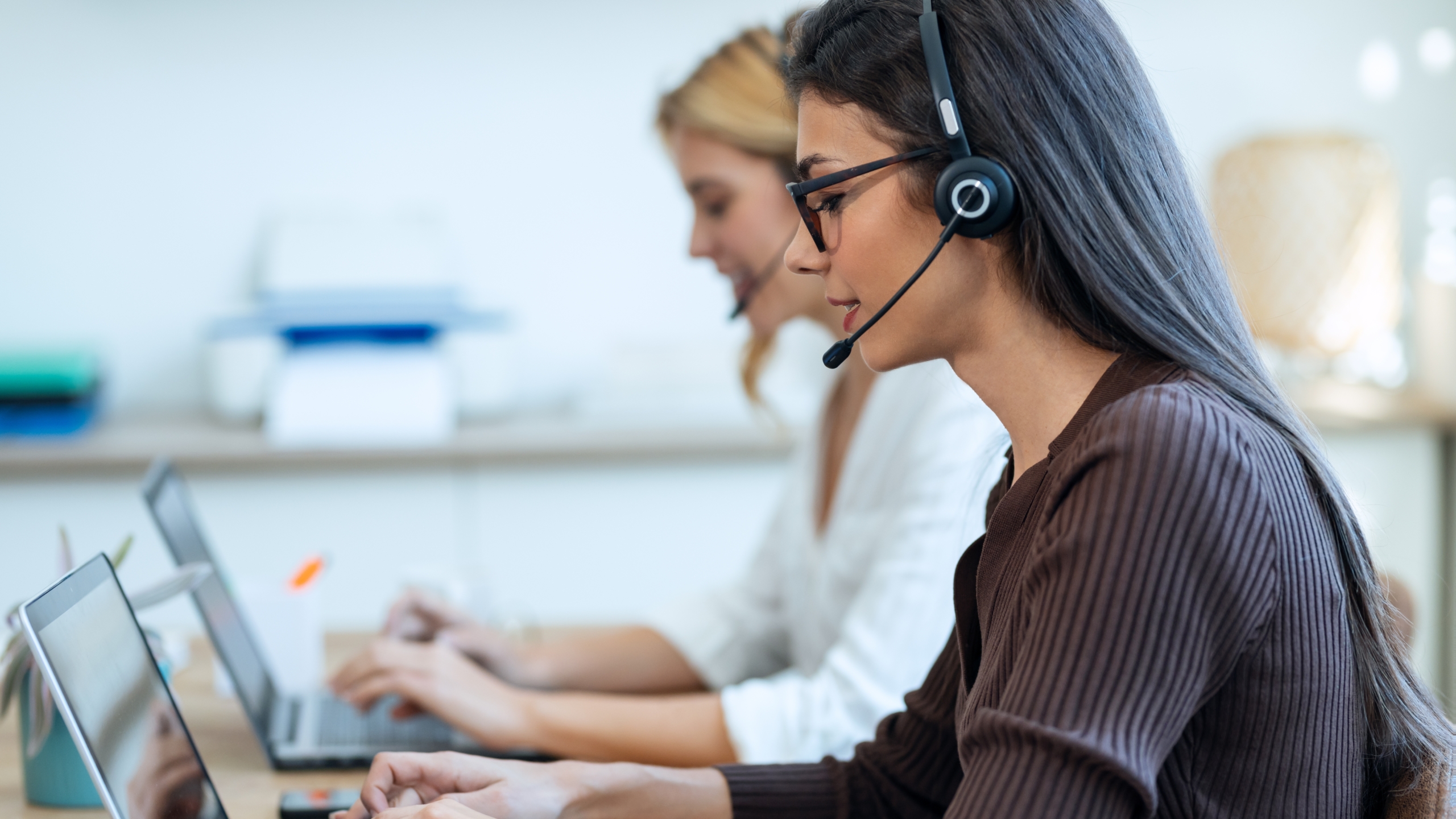 Female contact centre workers with headsets, speaking on a call using a UCaaS solution. 