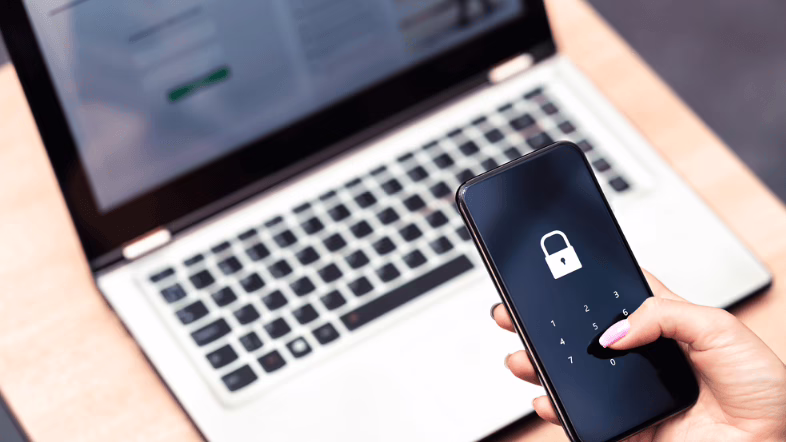 A person using a password-locked smartphone alongside a laptop, illustrating the importance of network security when comparing SD-WAN and VPN solutions for business