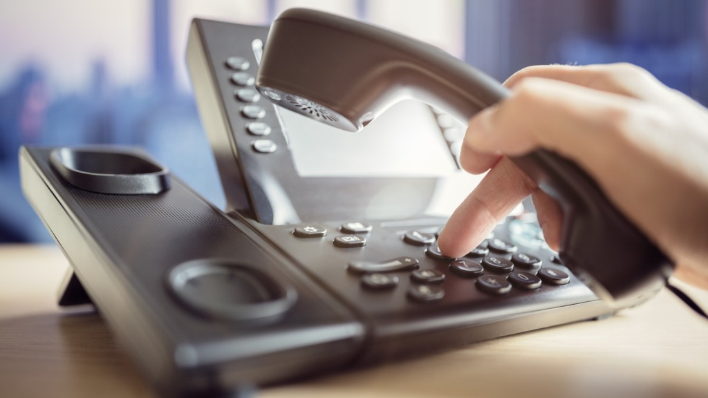 Hand holding receiver of a landline phone handset, dialling phone number into keypad