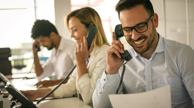 Business employees using desk phones to communicate in an office, demonstrating unified communications enhancing messaging between staff and HR departments