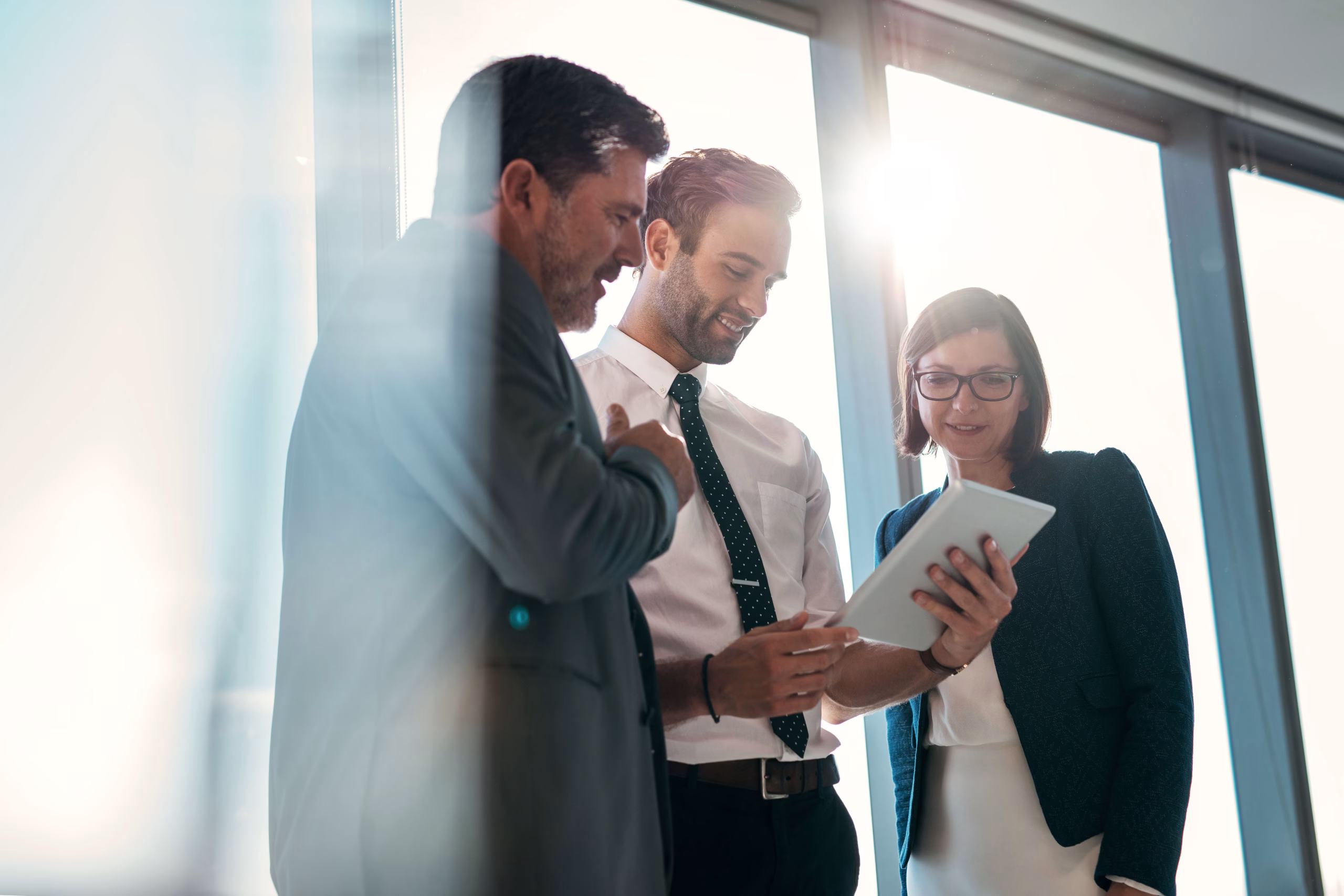 Three business professionals collaborating around a tablet in a modern office, representing Elite Group's business technology and communications solutions